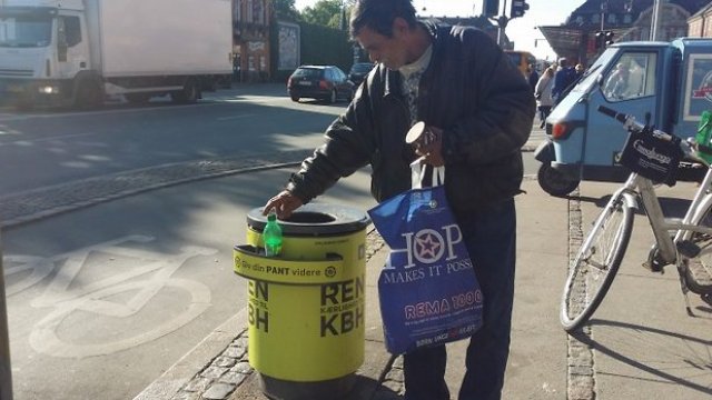 Image of man picking up bottle from "pant"/"pfand" holder on trashbin