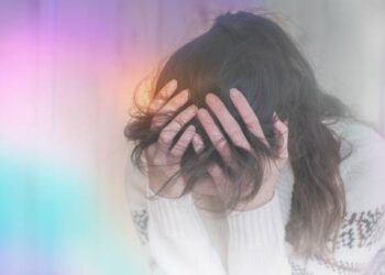 Person holding their head in pain showing and covering their face in them.